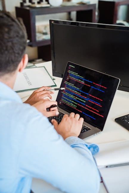 A close-up photograph of a laptop on a wooden surface displaying lines of code on its screen, with a beige ceramic mug partially visible to the right. The mug has black printed text that reads 'This c
